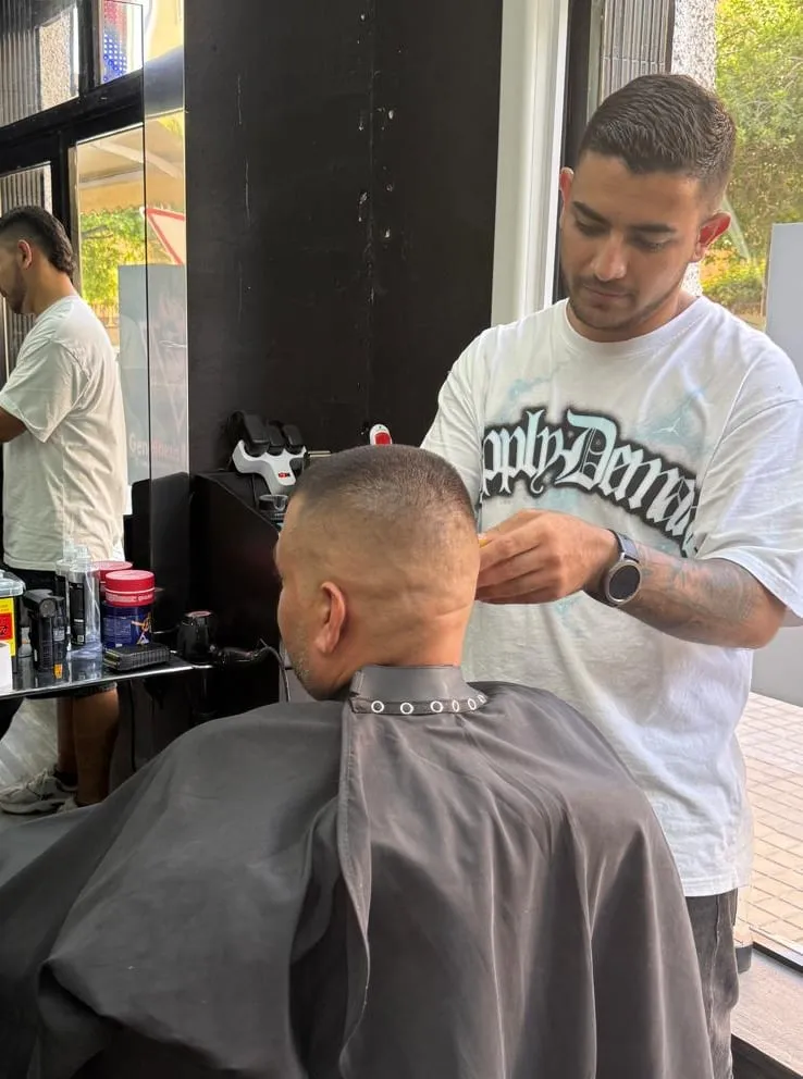 Jarol cortando el pelo a un cliente en la barbería